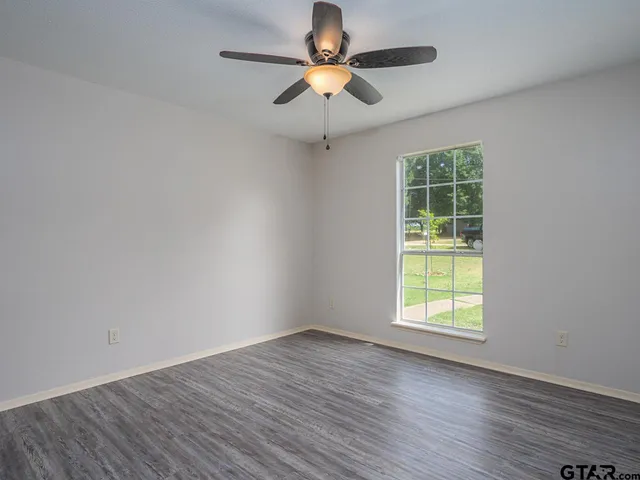 an empty room with wooden floor chandelier fan and windows
