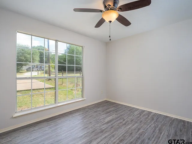 an empty room with wooden floor fan and windows
