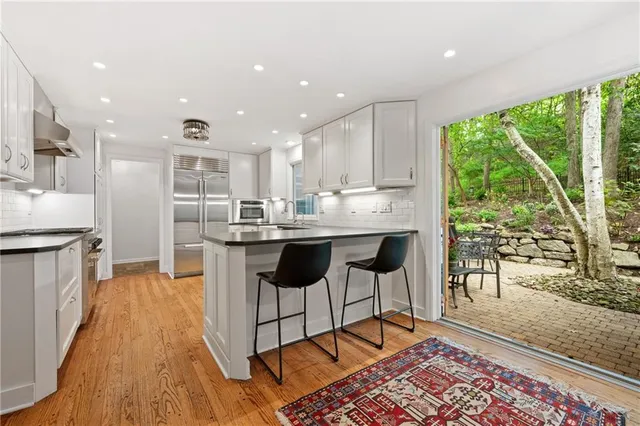 a kitchen with stainless steel appliances granite countertop a stove a refrigerator a sink a dining table and chairs with wooden floor