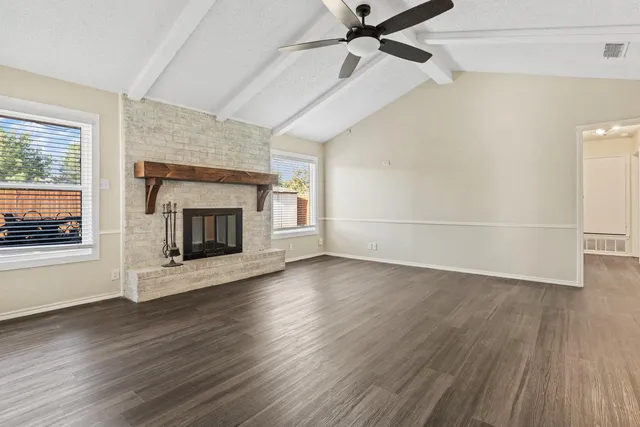 an empty room with wooden floor fireplace and windows