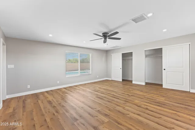 a view of an empty room with wooden floor and a ceiling fan