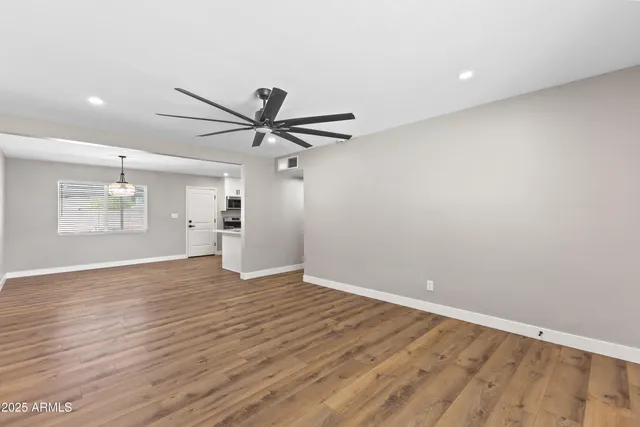 a view of an empty room with wooden floor and a ceiling fan