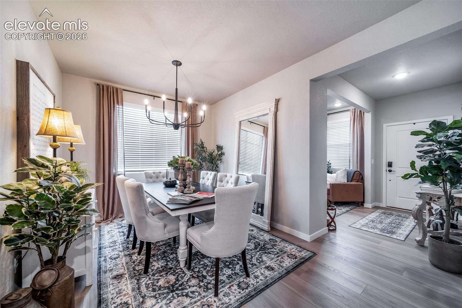 4876 Truscott Road Colorado Springs, CO 80925 - Photo 13 of 28 Dining area featuring a contemporary chandelier, wood-finish flooring, white baseboards, and a large window with blinds
*Photos of a model home*