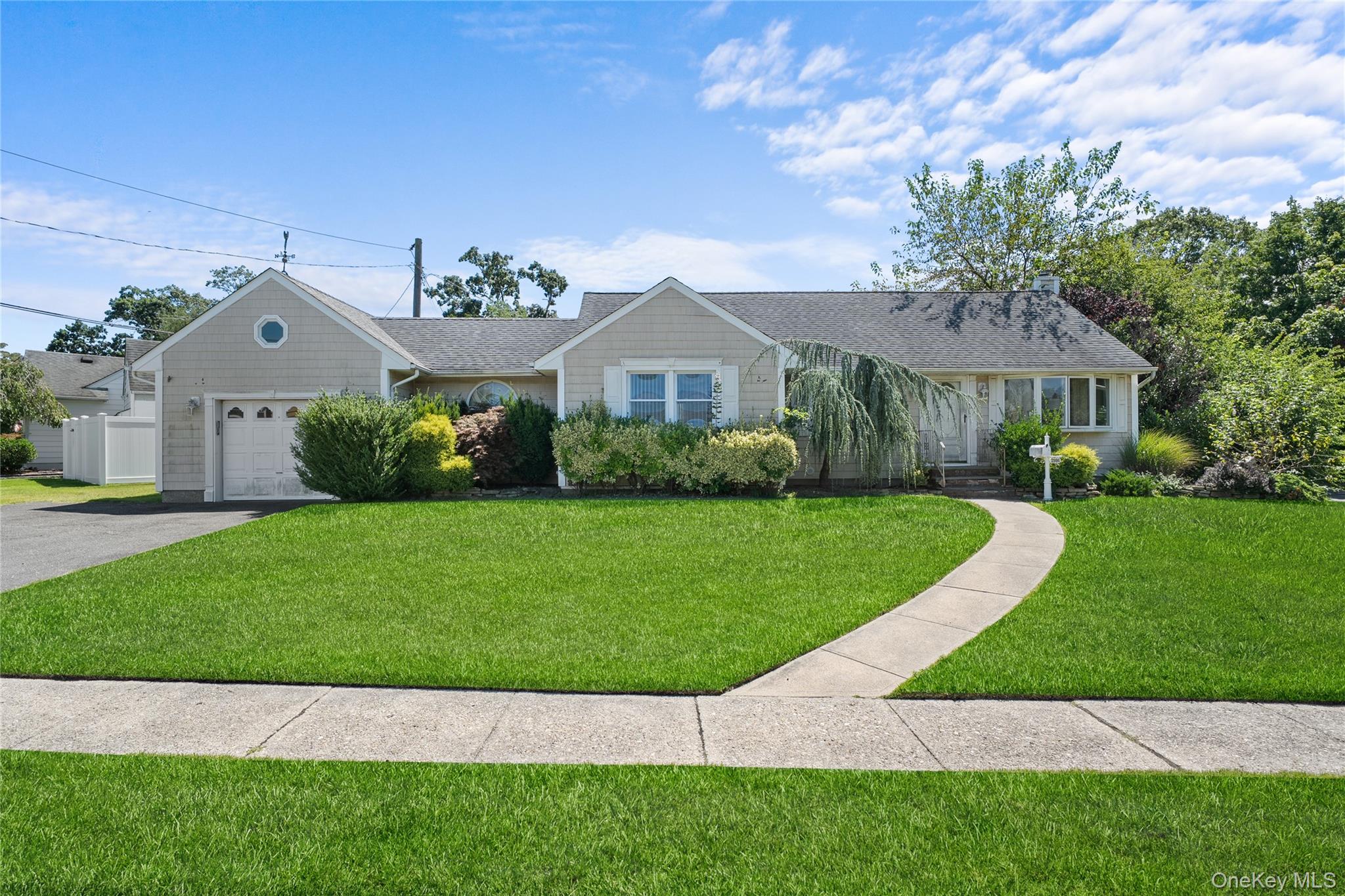 Ranch-style home featuring an attached garage, roof with shingles, a front yard, and asphalt driveway