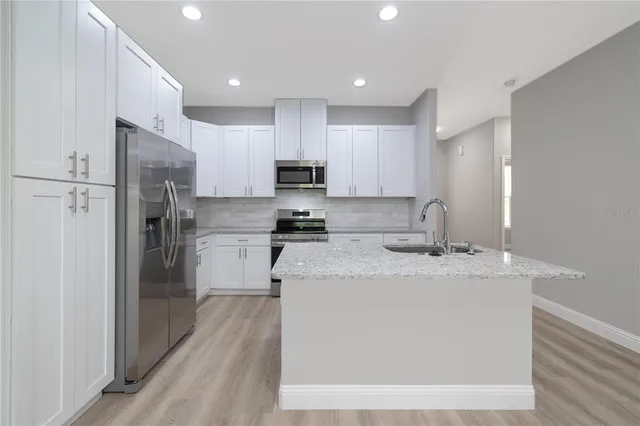 a large kitchen with stainless steel appliances granite countertop a refrigerator a oven a sink and white cabinets with wooden floor