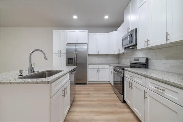 a kitchen with stainless steel appliances granite countertop a sink stove refrigerator and cabinets