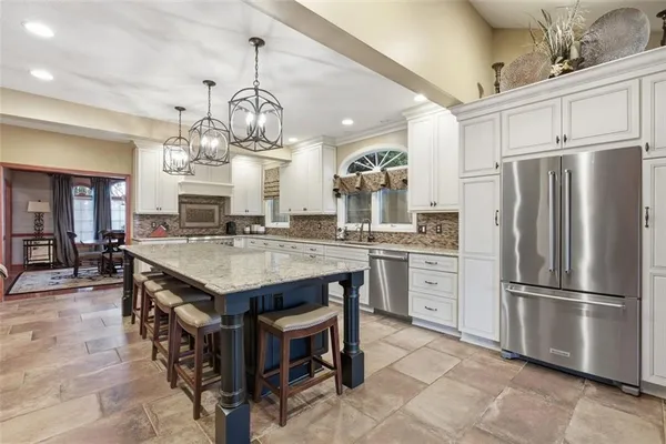 a kitchen with stainless steel appliances granite countertop a refrigerator a sink dishwasher a dining table and chairs with wooden floor