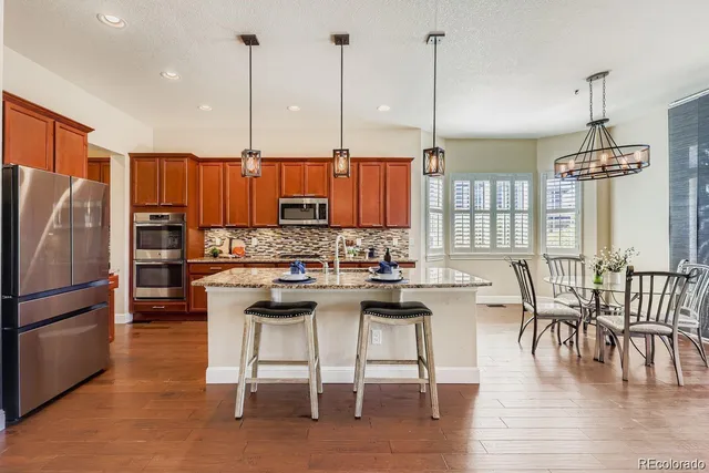 a kitchen with stainless steel appliances granite countertop a stove a refrigerator a kitchen island a dining table and chairs