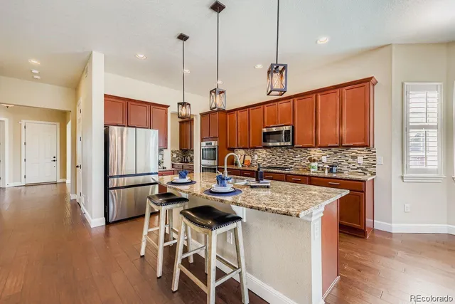 a kitchen with stainless steel appliances granite countertop a stove top oven a refrigerator a sink and white cabinets with wooden floor