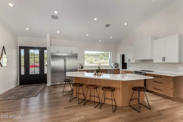 a kitchen with stainless steel appliances granite countertop a kitchen island a stove a refrigerator a sink a dining table and chairs with wooden floor