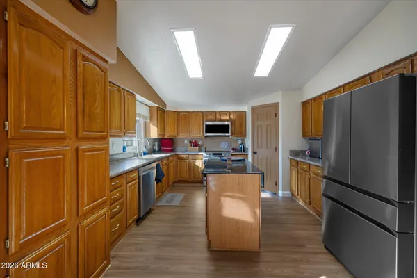 a kitchen with stainless steel appliances granite countertop a refrigerator a stove top oven a sink dishwasher and wooden cabinets with wooden floor