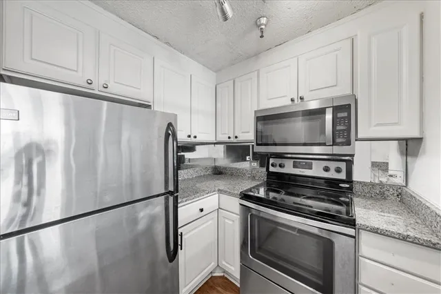 a kitchen with granite countertop a refrigerator stove and white cabinets