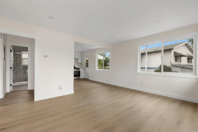 an empty room with wooden floor and a kitchen