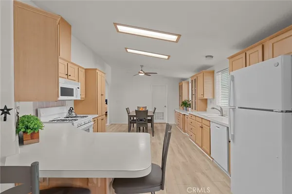 a white kitchen with stainless steel appliances a refrigerator a stove a sink dishwasher and white cabinets with wooden floor