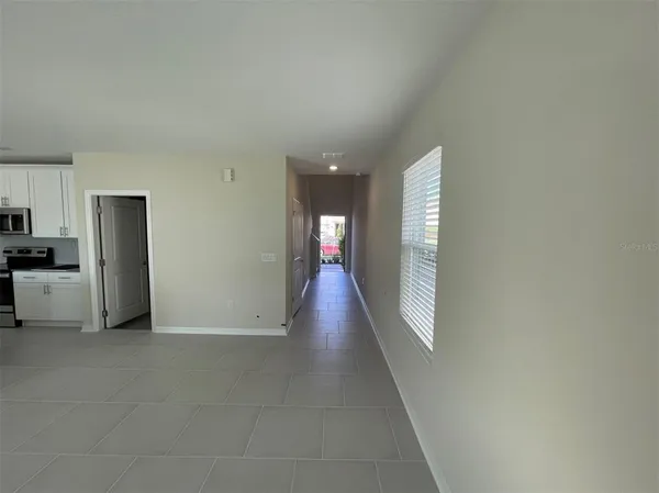 a view of a hallway to an empty room with wooden floor and a kitchen