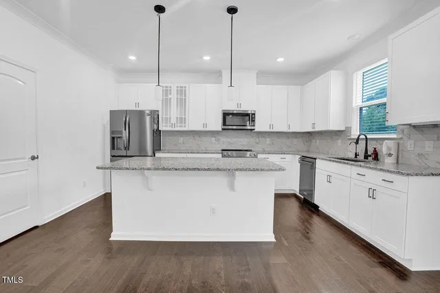 a kitchen with stainless steel appliances granite countertop a sink a stove a refrigerator a center island and wooden floor