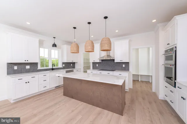 a large kitchen with stainless steel appliances kitchen island granite countertop a stove a sink a refrigerator and white cabinets with wooden floor