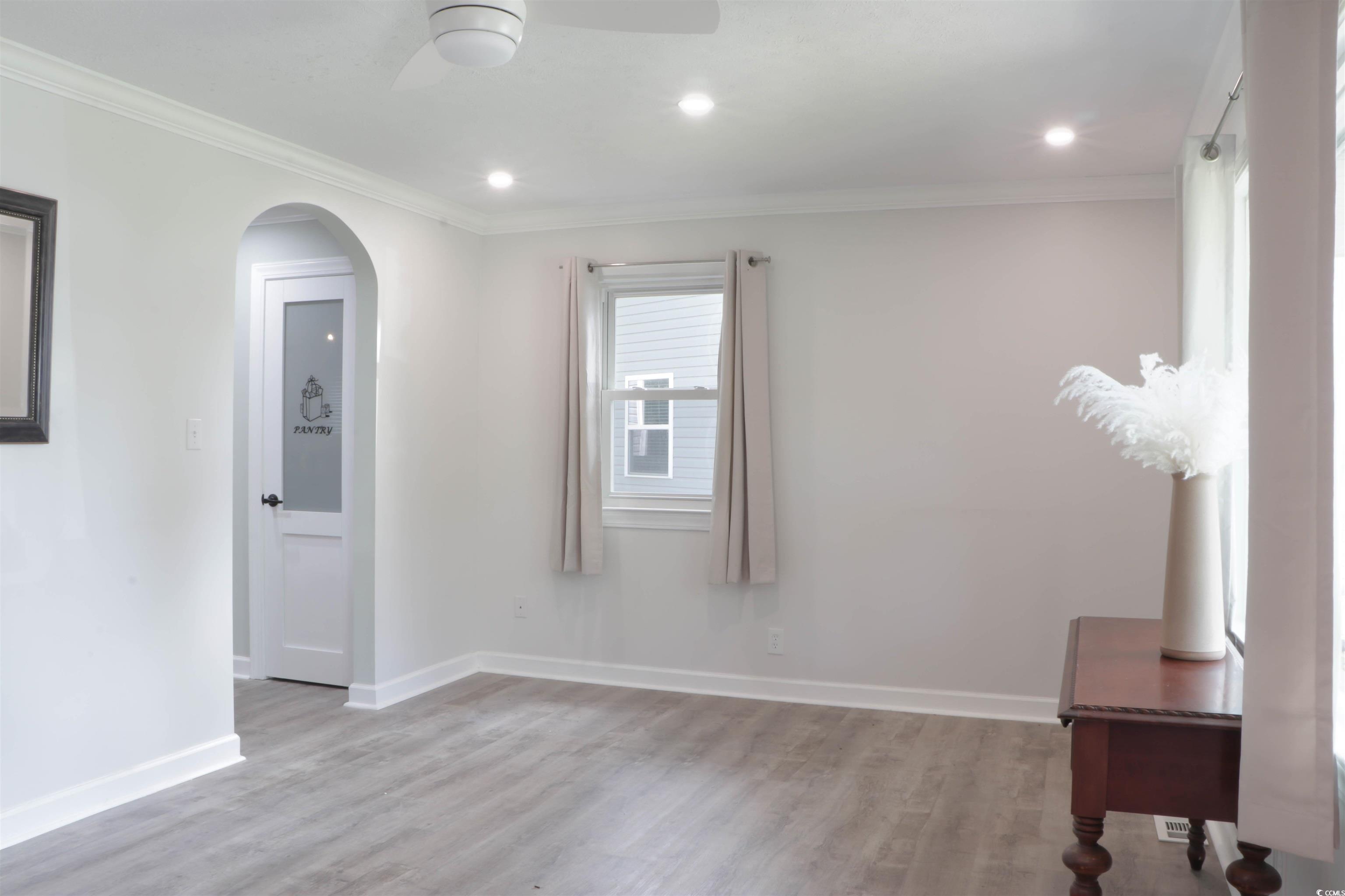 1014 Bay Drive Surfside Beach, SC 29575 - Photo 5 of 27 Unfurnished room with ceiling fan, light wood finished floors, crown molding, arched walkways, and baseboards