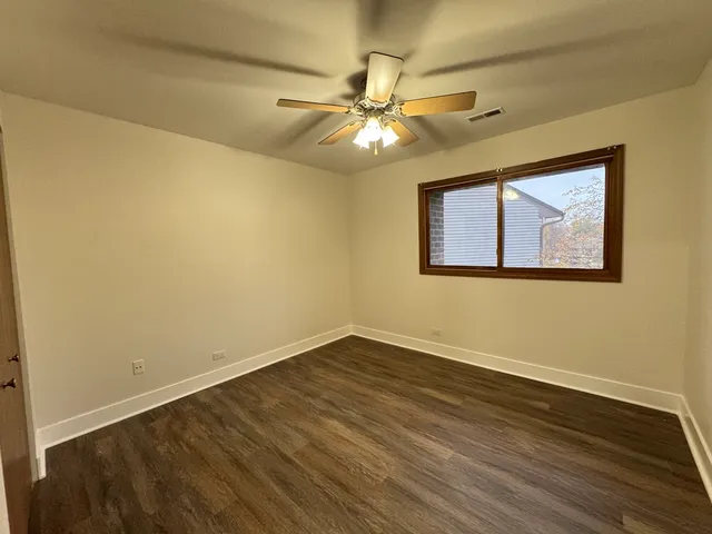 a view of an empty room with wooden floor and a ceiling fan