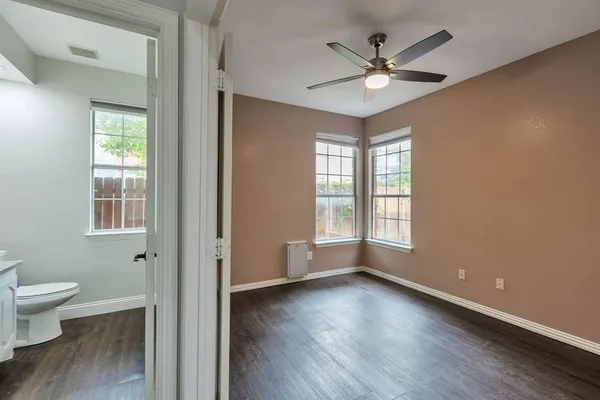 an empty room with wooden floor chandelier fan and windows