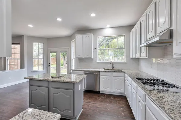 a kitchen with stainless steel appliances granite countertop a stove a sink dishwasher a refrigerator and white cabinets with wooden floor