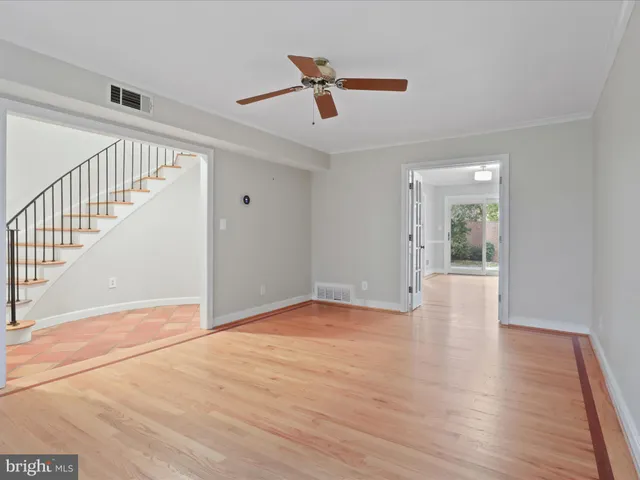 a view of an empty room with wooden floor and a ceiling fan