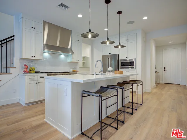 a kitchen with stainless steel appliances granite countertop a sink a stove a refrigerator and island with wooden floor