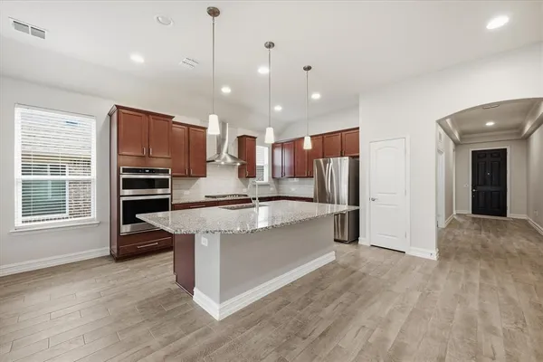 a large kitchen with kitchen island a stove a sink a refrigerator and a granite counter tops with wooden floors