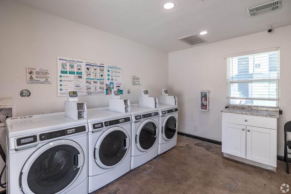 301 Rolston Road, Unit 303101 Irving, TX 75060 - Photo 4 of 4 On-site laundry facility featuring multiple front-load washing machines, a window with blinds, recessed lighting, and a white cabinet with a stone-look countertop