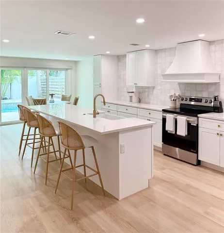 a kitchen with stainless steel appliances granite countertop a stove a sink a refrigerator and a dining table with white cabinets