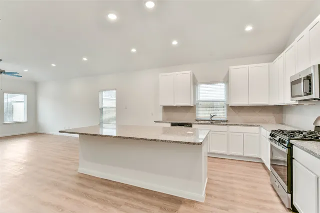 a large kitchen with stainless steel appliances granite countertop a stove a sink and a white countertops with wooden floor