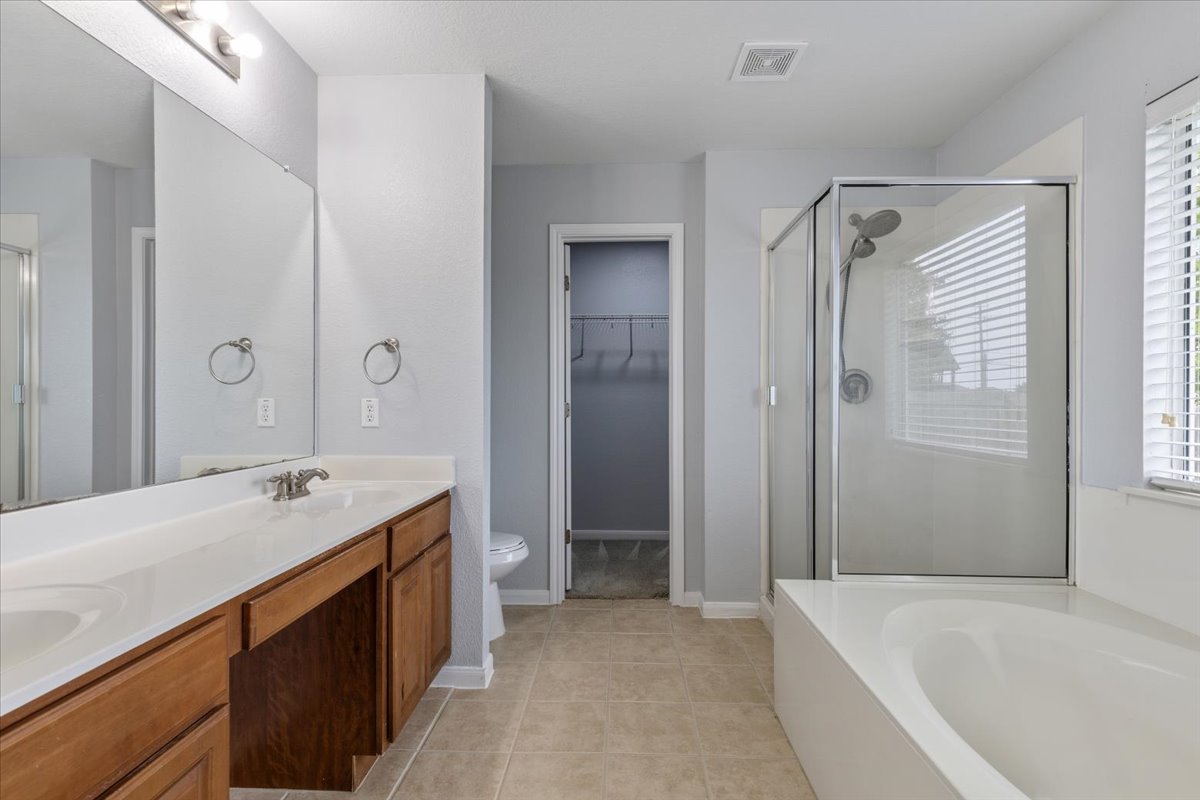 17812 Masi Loop Pflugerville, TX 78660 - Photo 22 of 38 Bathroom featuring a dual-sink vanity with wood-finish cabinetry, a large frameless mirror, a glass-enclosed shower, a separate built-in bathtub, and horizontal window blinds
