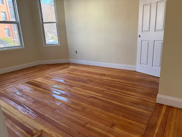 a view of an empty room with wooden floor and a window