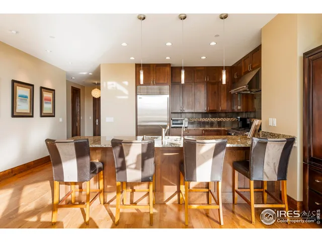 a kitchen with stainless steel appliances kitchen island granite countertop a dining table chairs and a refrigerator