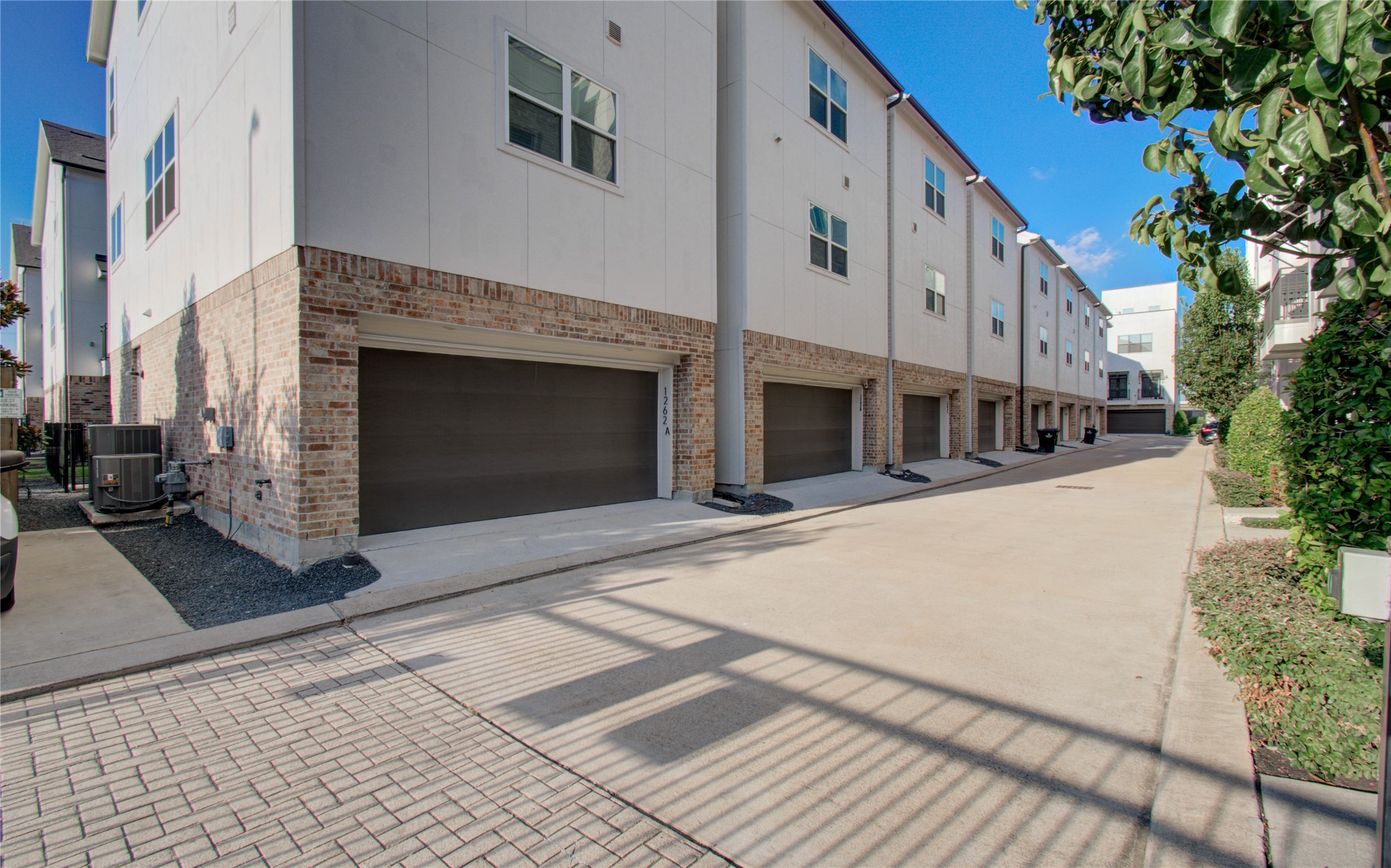1262 North Post Oak Road, Unit A Houston, TX 77055 - Photo 7 of 50 The rear exterior view shows a clean, paved alleyway providing direct access to double-car garage bays for each townhome. Sturdy brick accents and subtle exterior lighting enhance the functionality and security of the back entrance.