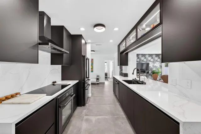 a large kitchen with stainless steel appliances a sink dishwasher a stove and a refrigerator with wooden floor