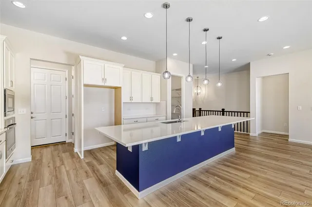 a large kitchen with stainless steel appliances a large counter top a sink a refrigerator and a wooden floor