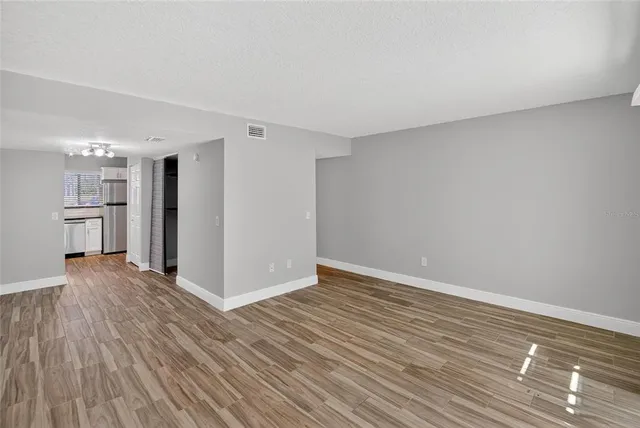 a view of empty room with wooden floor and kitchen