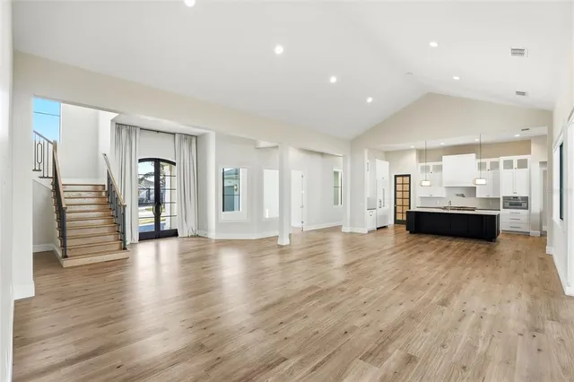 a view of an empty room with wooden floor and kitchen space with a sink