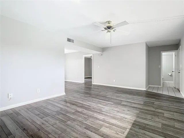 a view of an empty room with wooden floor and a ceiling fan