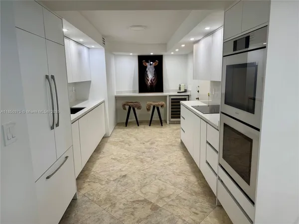 a large white kitchen with stainless steel appliances kitchen island granite countertop a stove a sink and a microwave