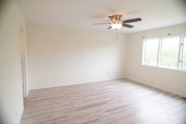 an empty room with wooden floor fan and windows