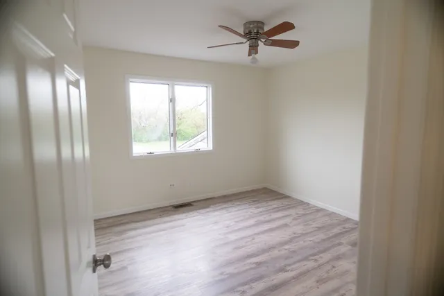 a view of empty room with wooden floor and fan
