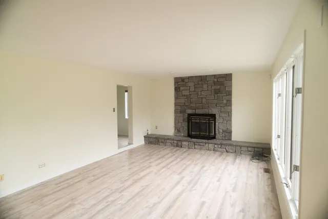 a view of an empty room with wooden floor fireplace and a window