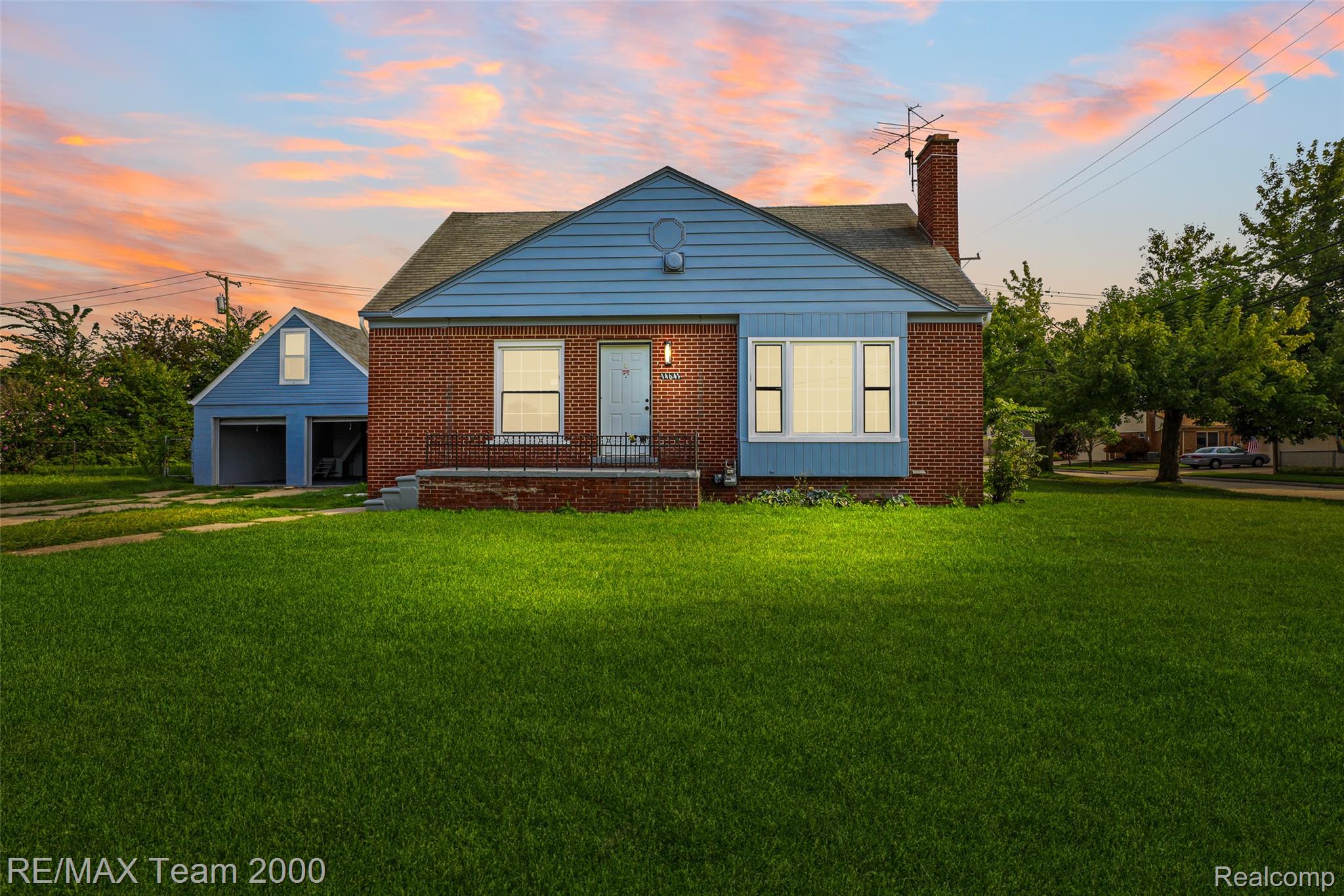 Brick exterior with blue siding accents, front entry with wrought iron railing, and a detached two-car garage