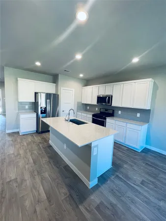 a large white kitchen with kitchen island a sink dishwasher a oven and a large island with wooden floor