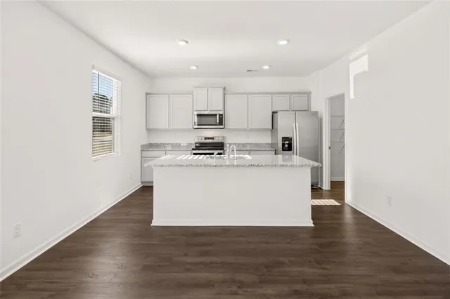 a view of kitchen with stainless steel appliances granite countertop a stove a refrigerator a sink and white cabinets with wooden floor