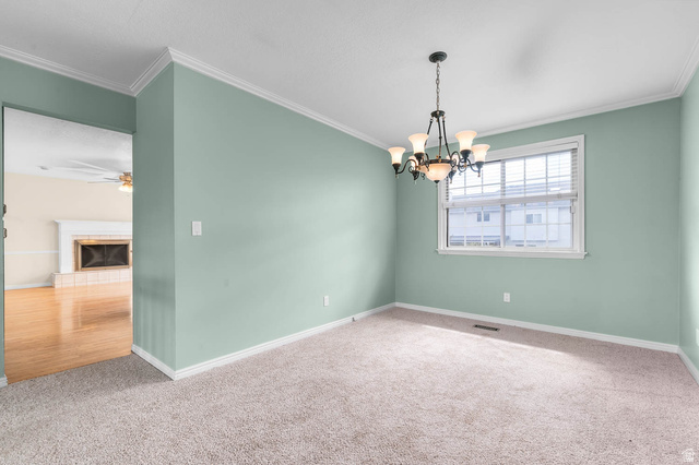1822 East 9800th Street South Sandy, UT 84092 - Photo 27 of 38 Carpeted empty room with crown molding, a tiled fireplace, a ceiling fan, and a chandelier