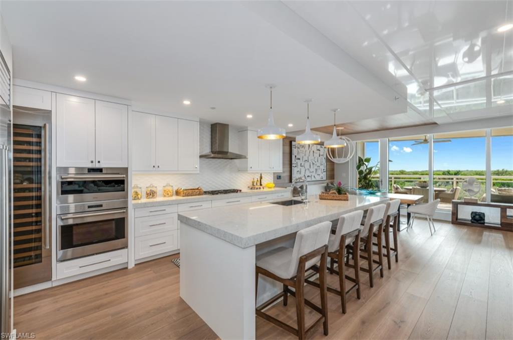13925 Old Coast Road, Unit 403 Naples, FL 34110 - Photo 9 of 24 Kitchen with white cabinetry, pendant lighting, a center island with sink, light stone countertops, and a kitchen breakfast bar