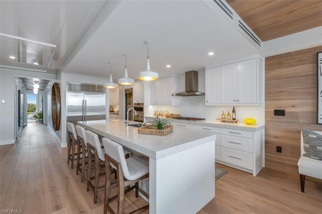 13925 Old Coast Road, Unit 403 Naples, FL 34110 - Photo 10 of 24 Kitchen featuring white cabinets, a kitchen bar, pendant lighting, a large island, and light stone countertops